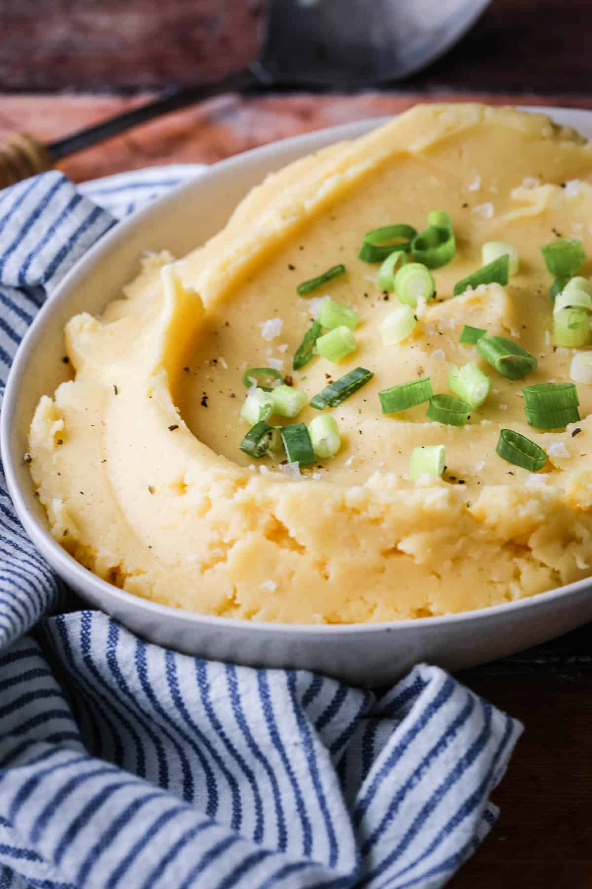 A bowl of cheesy mashed potatoes sprinkled with spring onions and flaked sea salt.