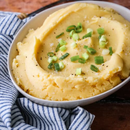 A bowl of cheesy mashed potatoes sprinkled with spring onions and flaked sea salt.