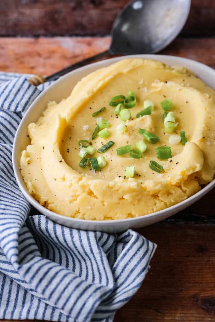 A bowl of cheesy mashed potatoes sprinkled with spring onions and flaked sea salt.