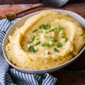A bowl of cheesy mashed potatoes sprinkled with spring onions and flaked sea salt.