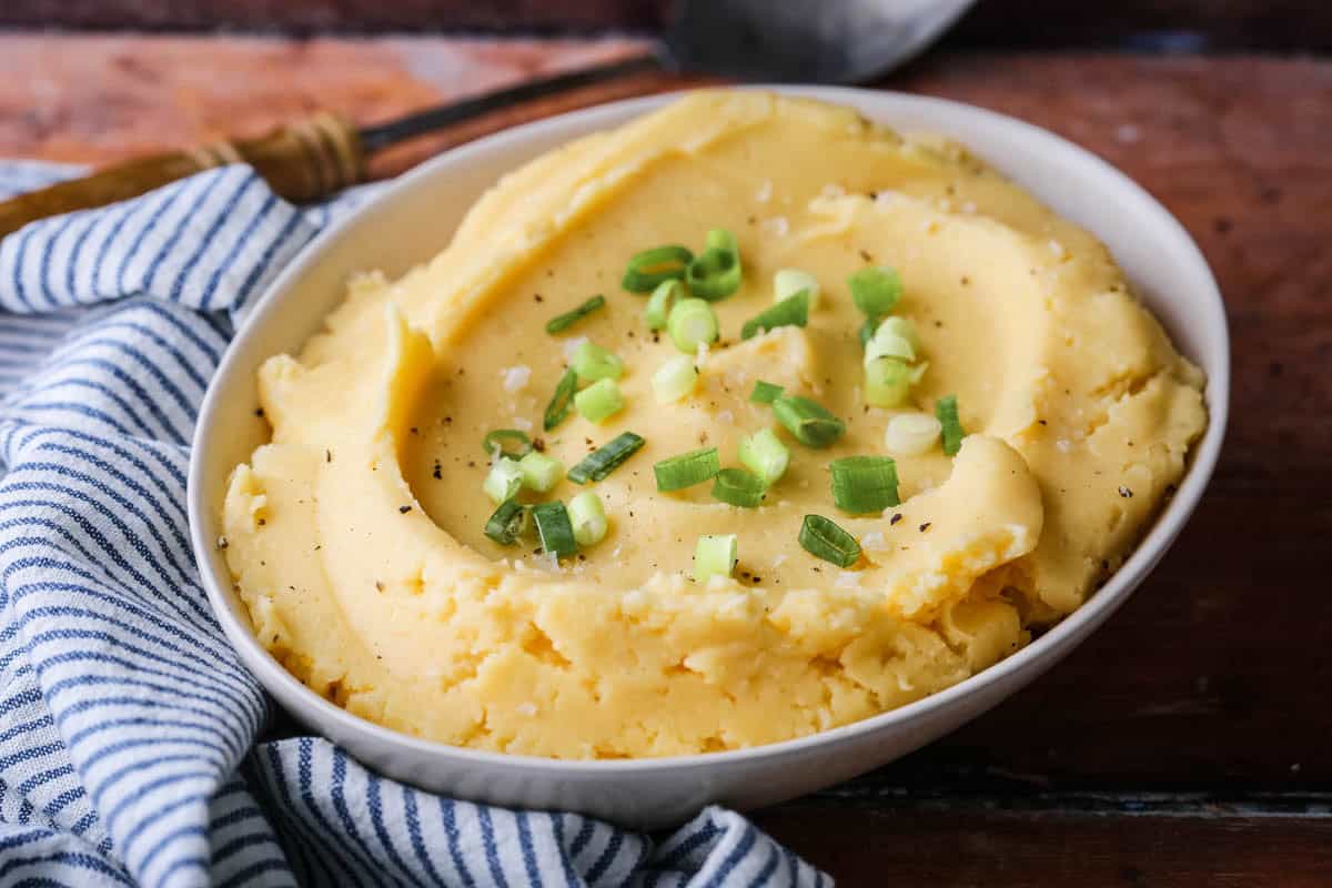 A bowl of cheesy mashed potatoes sprinkled with spring onions and flaked sea salt.