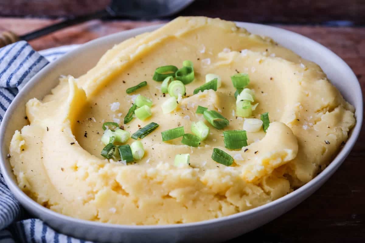 A bowl of cheesy mashed potatoes sprinkled with spring onions and flaked sea salt.
