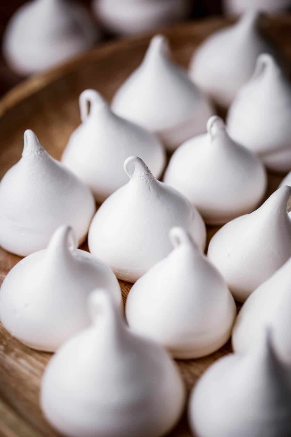 White Meringue Kisses on a wooden plate.