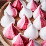Meringue Kisses with a swirl of red on a wooden plate.
