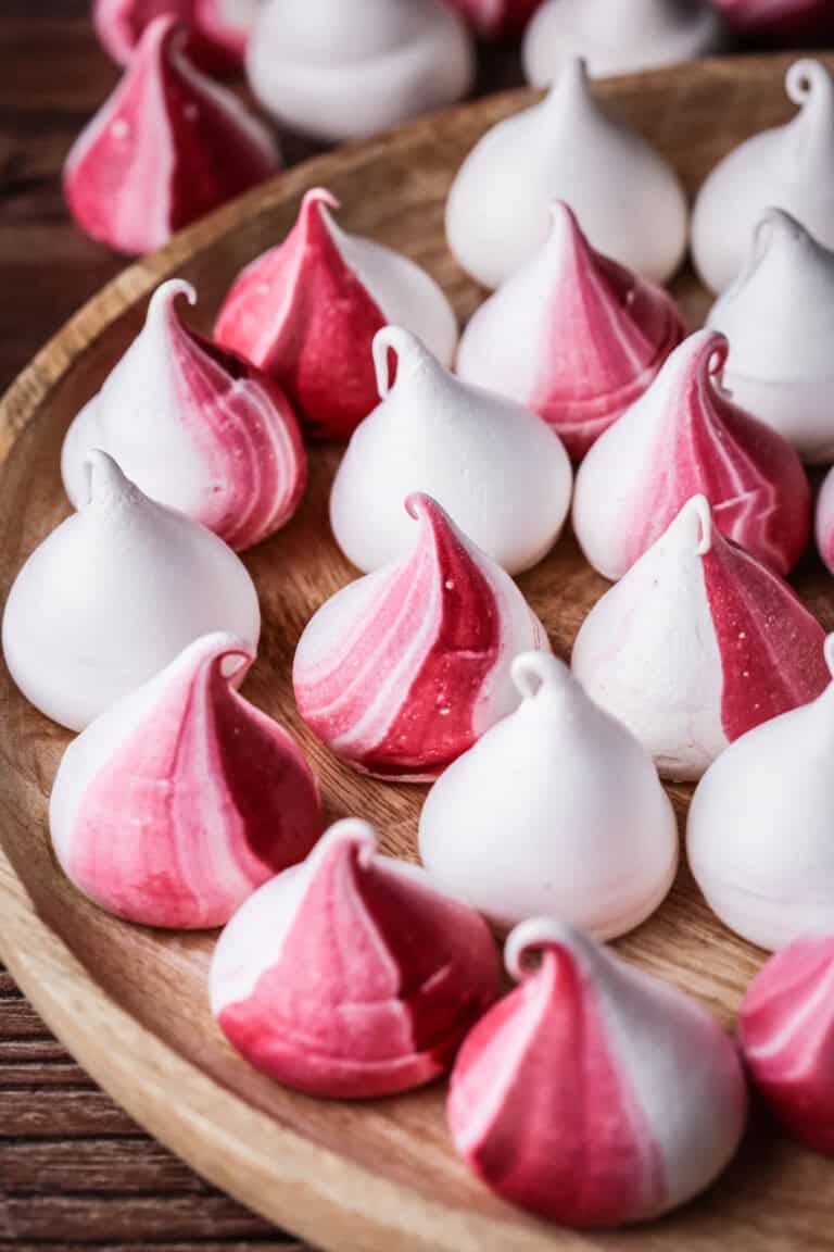 Meringue Kisses with a swirl of red on a wooden plate.