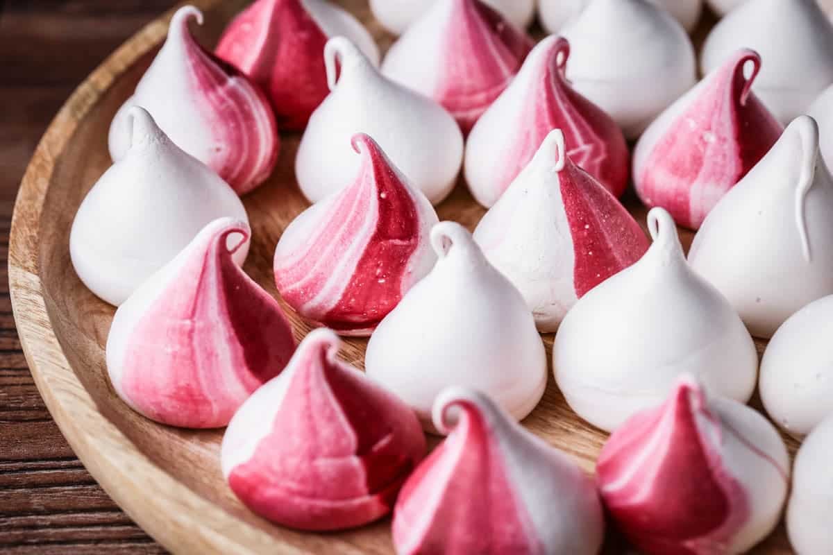 Meringue Kisses with a swirl of red on a wooden plate.