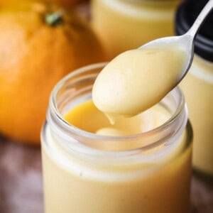 Spoon dipping into jar of freshly made orange curd showing thick ultra smooth preserve with a bright colour.