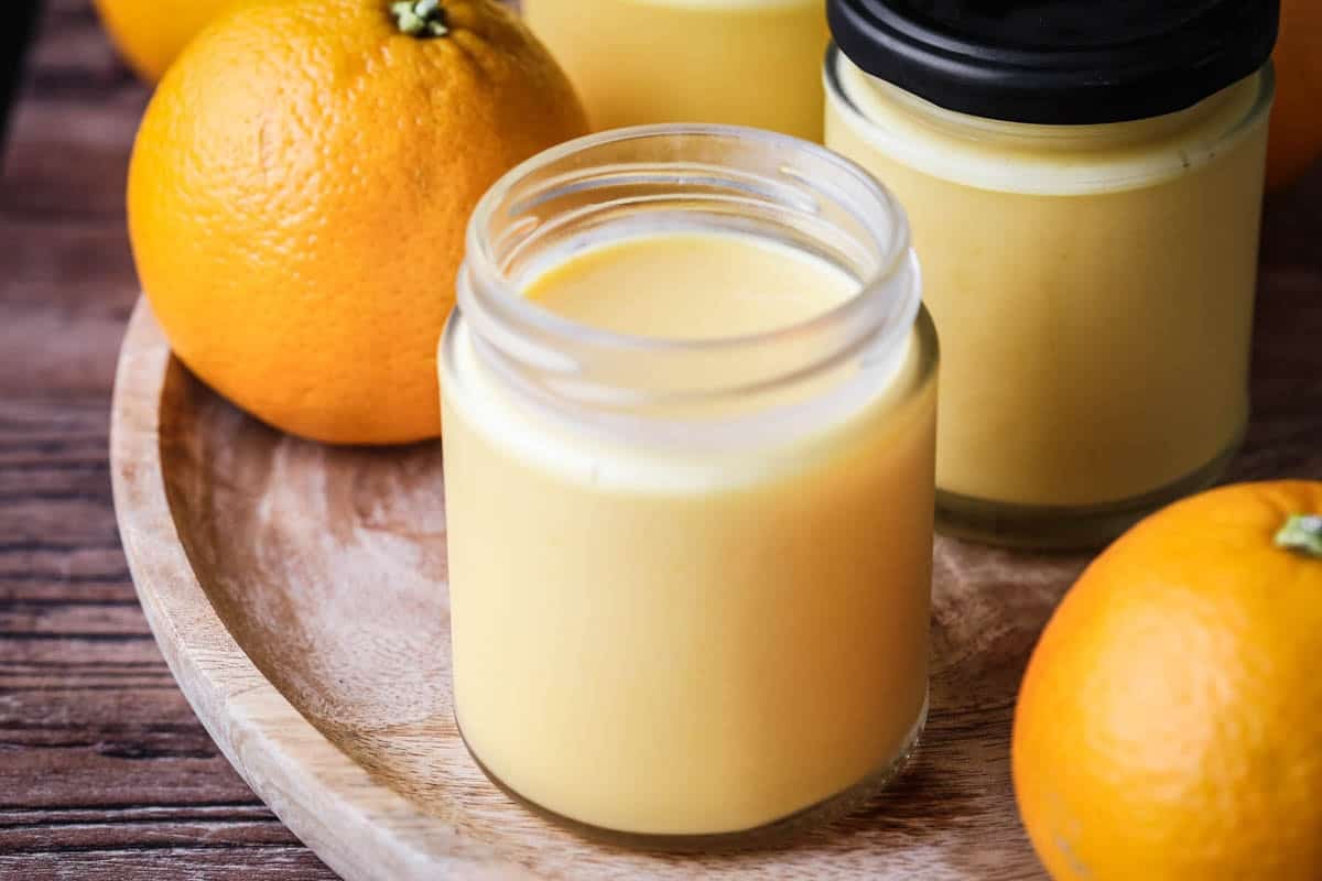 Jar of freshly made orange curd showing thick ultra smooth preserve with a bright colour.