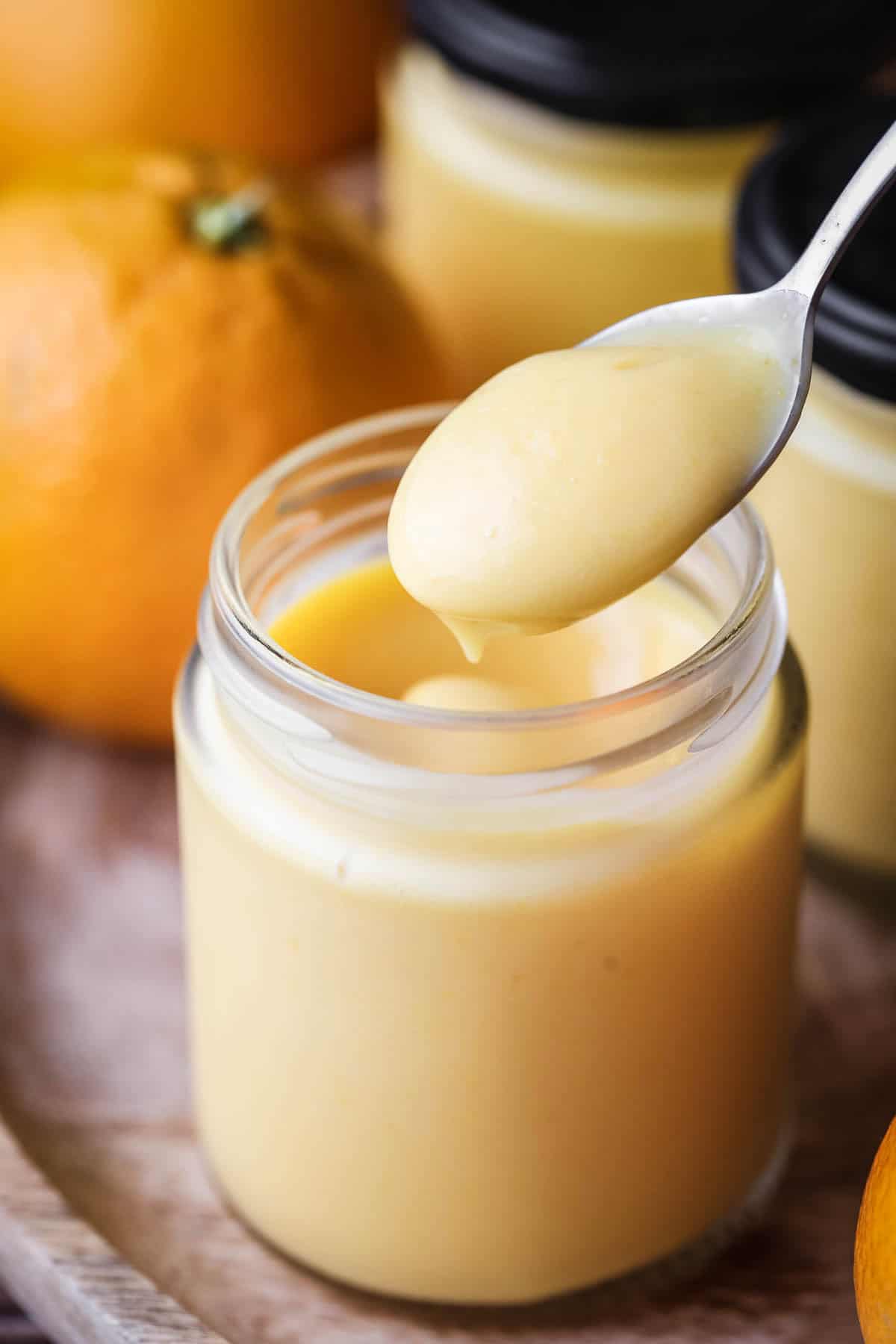 Spoon dipping into jar of freshly made orange curd showing thick ultra smooth preserve with a bright colour.