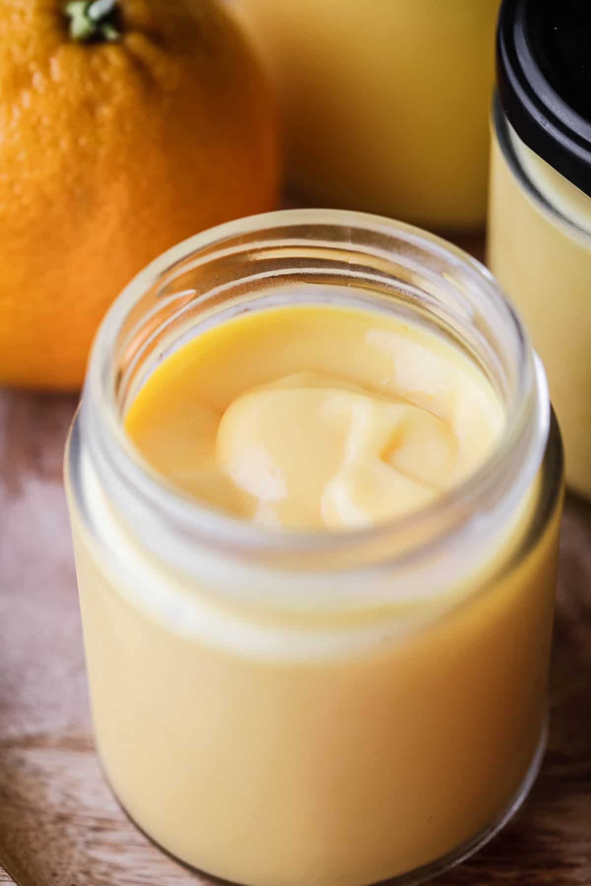 Jar of freshly made orange curd showing thick ultra smooth preserve with a bright colour.