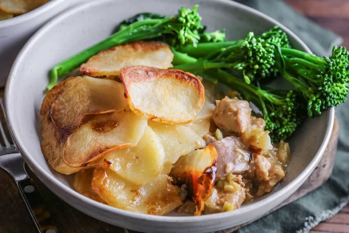 A bowl of Turkey Hotpot showing crisp potatoes and creamy turkey filling. Served with tenderstem broccoli.