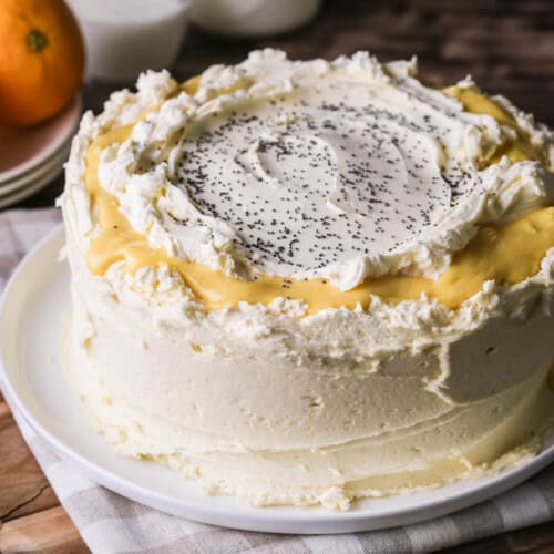 Gluten-Free Orange & Poppy Seed Cake on a plate. Thickly covered in a creamy buttercream icing with orange curd.