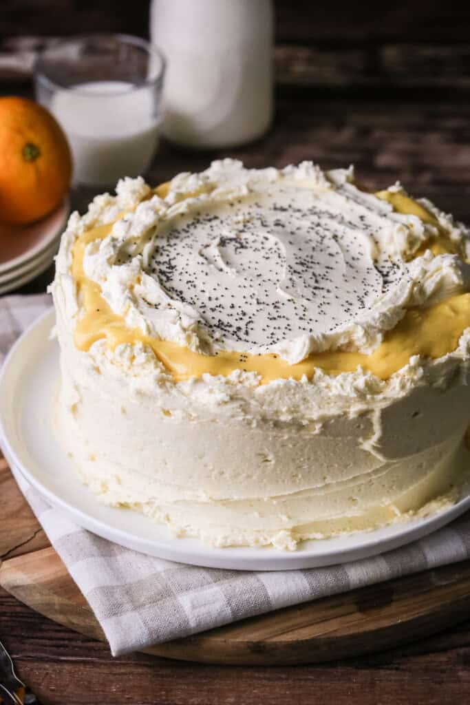Gluten-Free Orange & Poppy Seed Cake on a plate. Thickly covered in a creamy buttercream icing with orange curd.