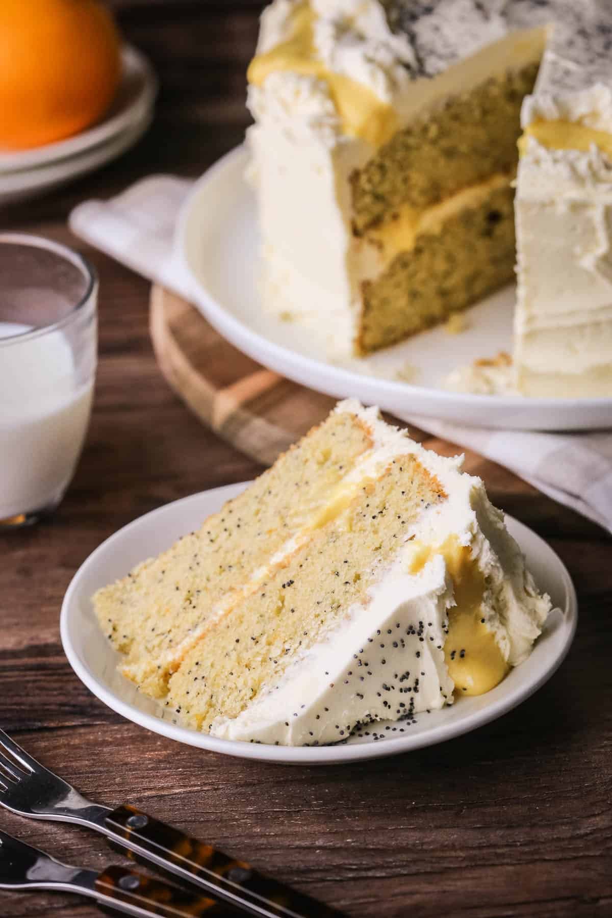 Slice of Gluten-Free Orange & Poppy Seed Cake on a plate showing thick layers of moist orange cake studded with poppy seeds, layered with fresh orange curd and buttercream.