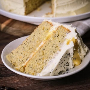 Slice of Gluten-Free Orange & Poppy Seed Cake on a plate showing thick layers of moist orange cake studded with poppy seeds, layered with fresh orange curd and buttercream.