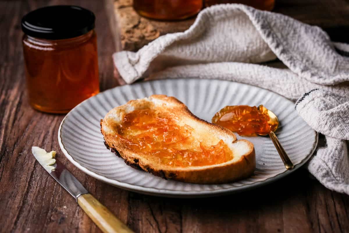 Seville Orange Marmalade on toast next to jar and a teaspoonful of marmalade.