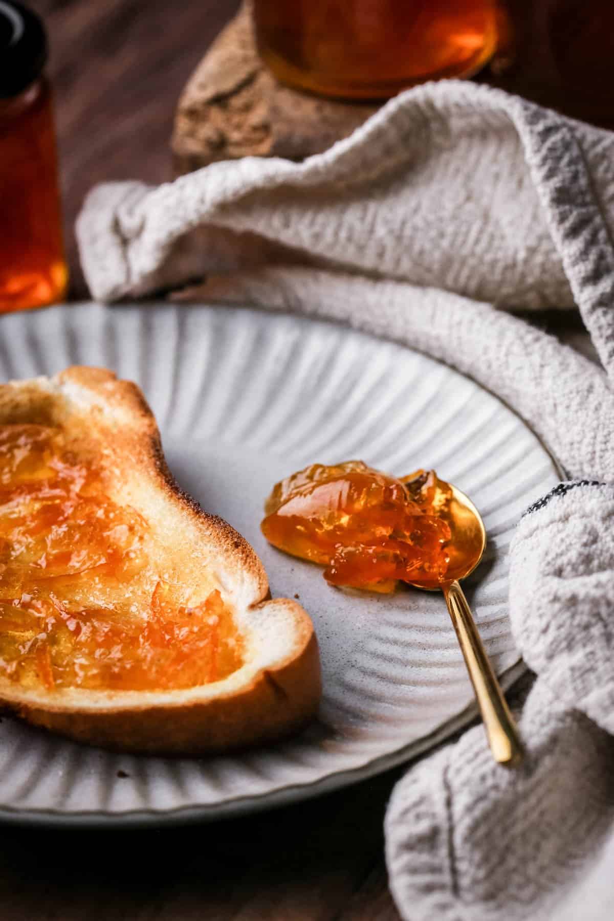 Seville Orange Marmalade on toast next to jar and a teaspoonful of marmalade.