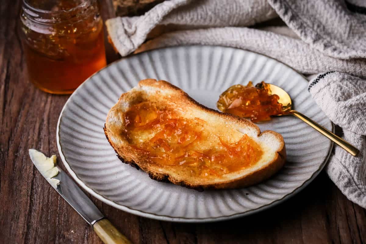 Seville Orange Marmalade on toast next to jar and a teaspoonful of marmalade.
