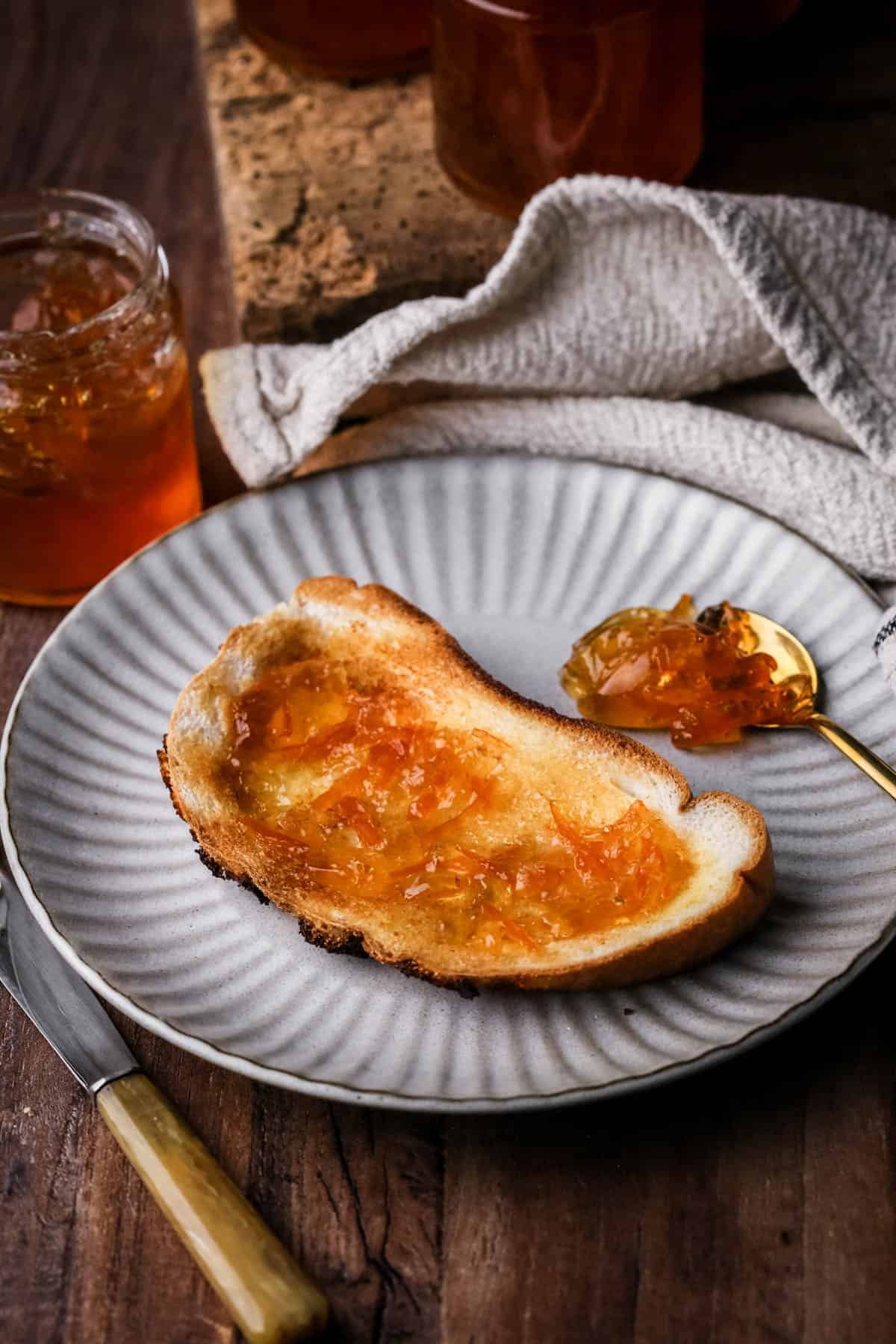 Seville Orange Marmalade on toast next to jar and a teaspoonful of marmalade.