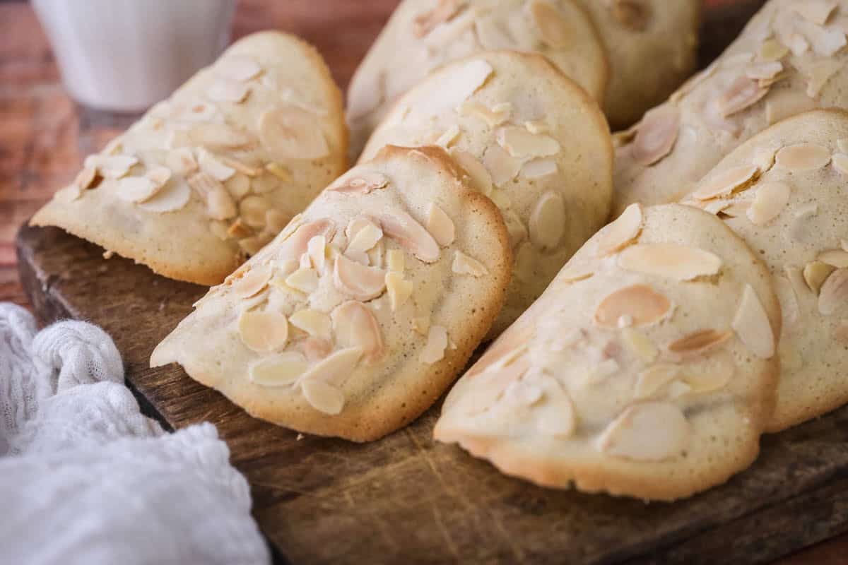 Gluten-Free Almond Tuile on a board golden crisp edges on the outside and paler in the centre, covered with flaked almonds.