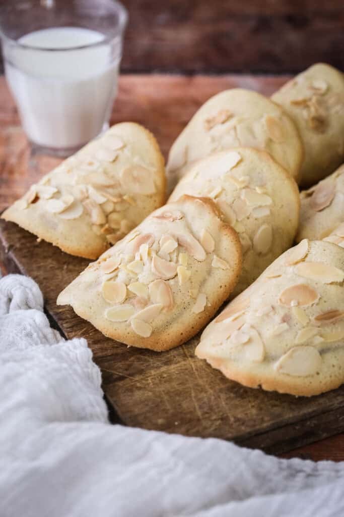 Gluten-Free Almond Tuile on a board golden crisp edges on the outside and paler in the centre, covered with flaked almonds.