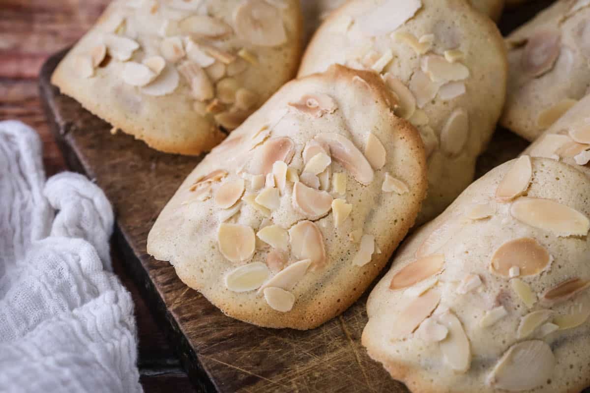 Gluten-Free Almond Tuile on a board golden crisp edges on the outside and paler in the centre, covered with flaked almonds.