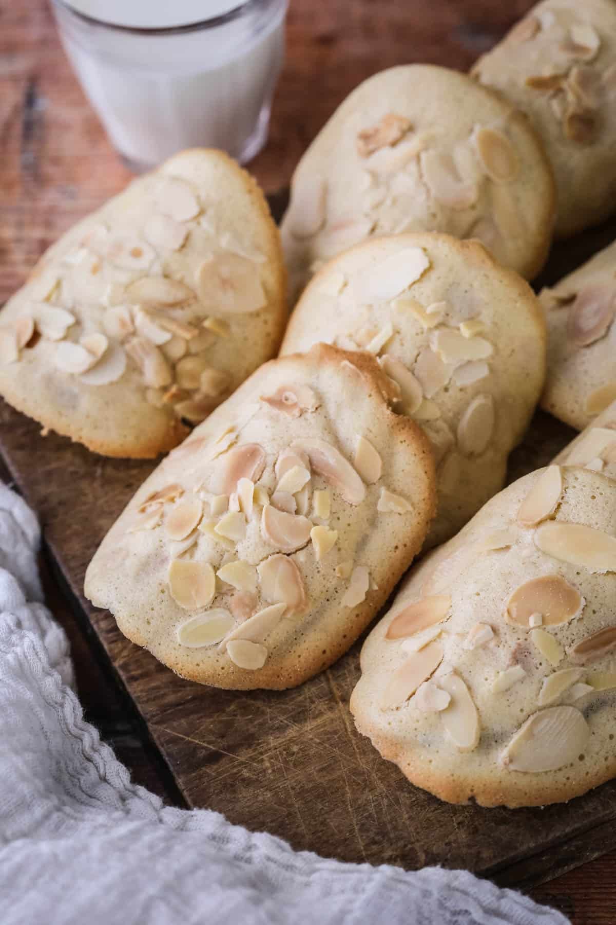 Gluten-Free Almond Tuile on a board golden crisp edges on the outside and paler in the centre, covered with flaked almonds.