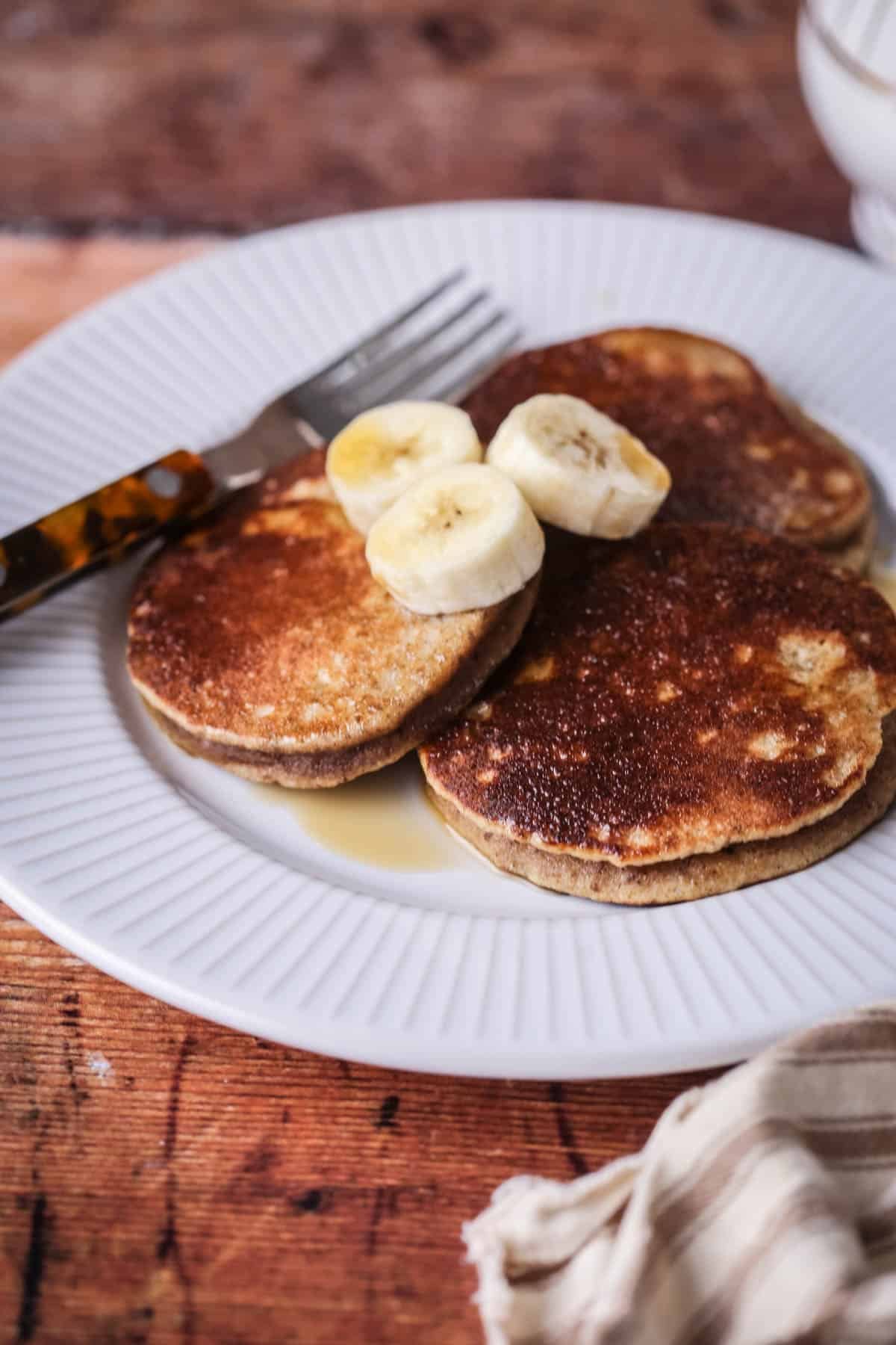 A plate of thick, soft and fluffy banana pancakes. Topped with bananas and drizzled with maple syrup.