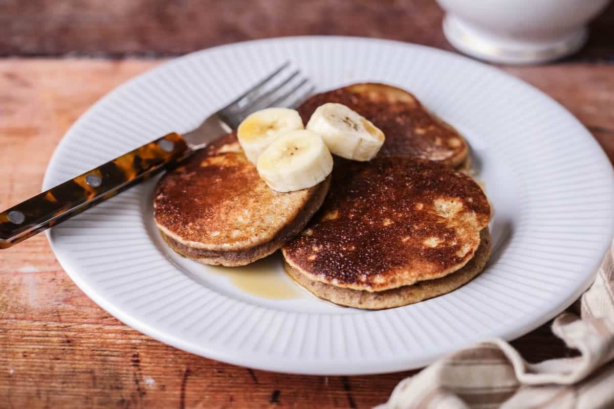 A plate of thick, soft and fluffy banana pancakes. Topped with bananas and drizzled with maple syrup.