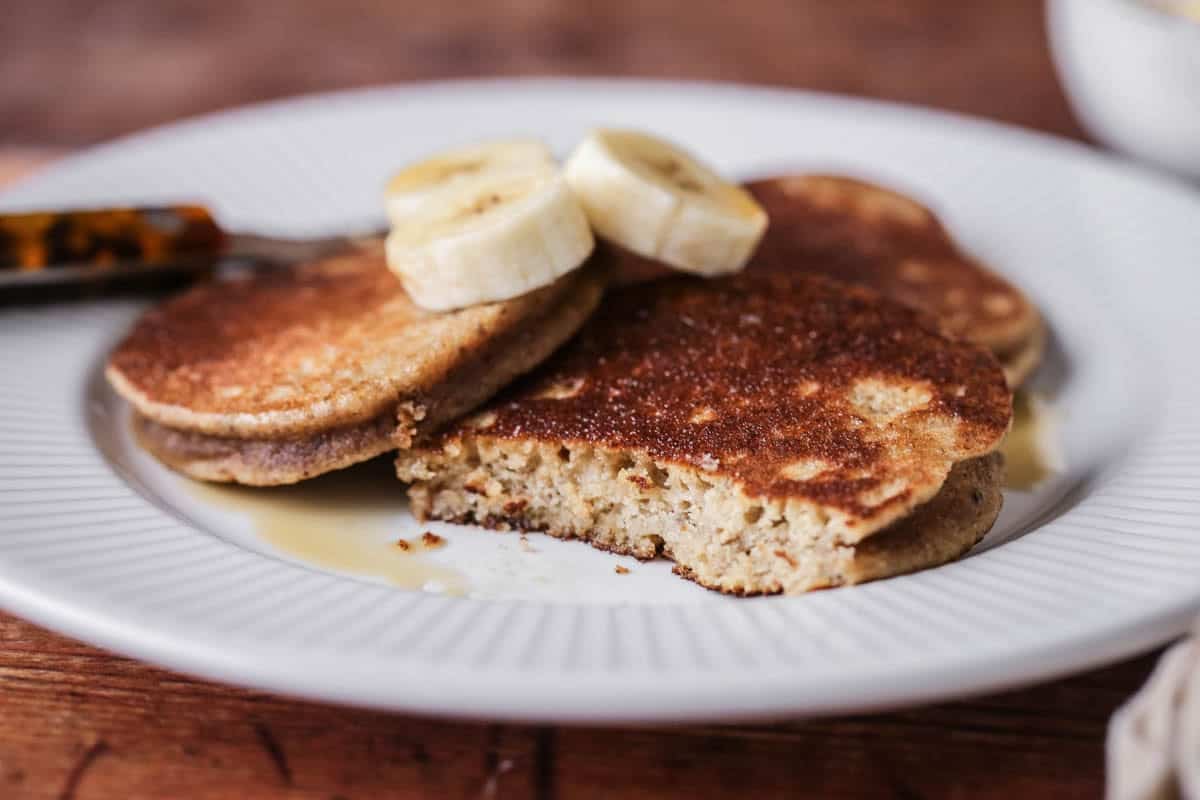 A plate of thick, soft and fluffy banana pancakes. Topped with bananas and drizzled with maple syrup.