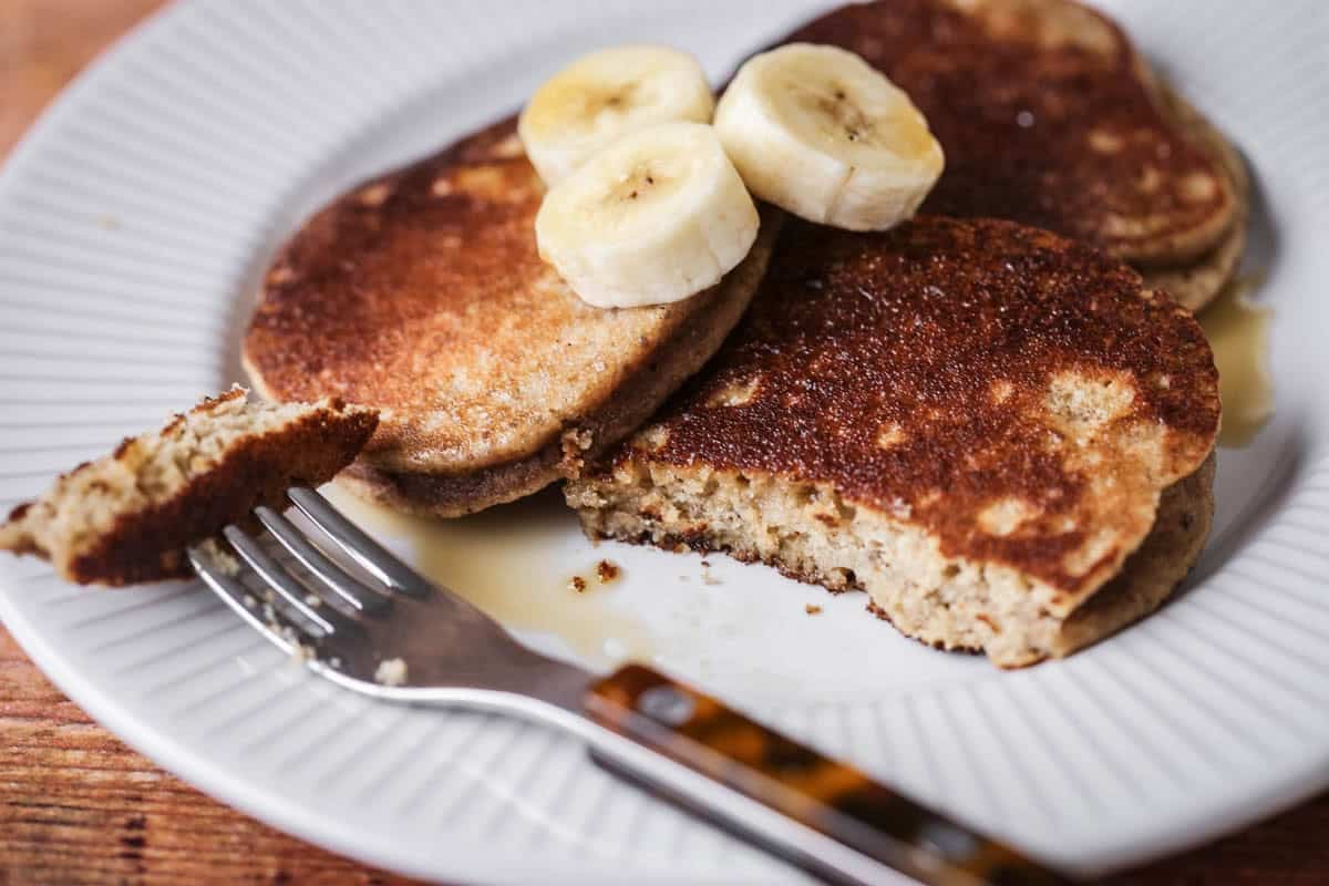 A plate of thick, soft and fluffy banana pancakes. Topped with bananas and drizzled with maple syrup.