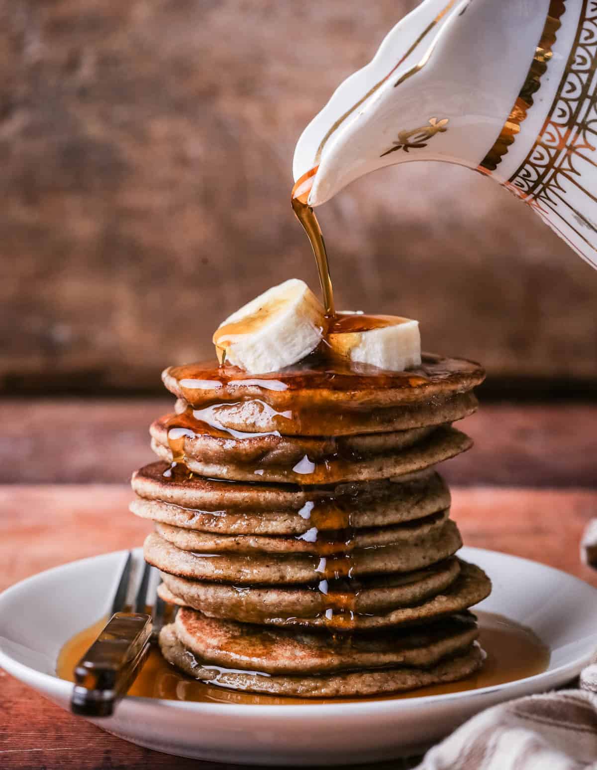 A stack of thick, soft and fluffy banana pancakes. Topped with bananas and drizzled with maple syrup.