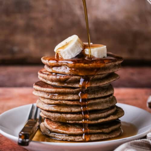 A stack of thick, soft and fluffy banana pancakes. Topped with bananas and drizzled with maple syrup.