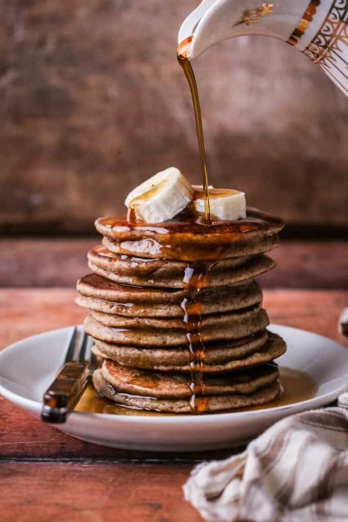 A stack of thick, soft and fluffy banana pancakes. Topped with bananas and drizzled with maple syrup.