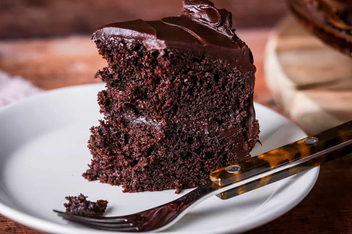 Forkful taken from slice of Chocolate fudge cake on plate showing soft moist sponge which holds together really well.