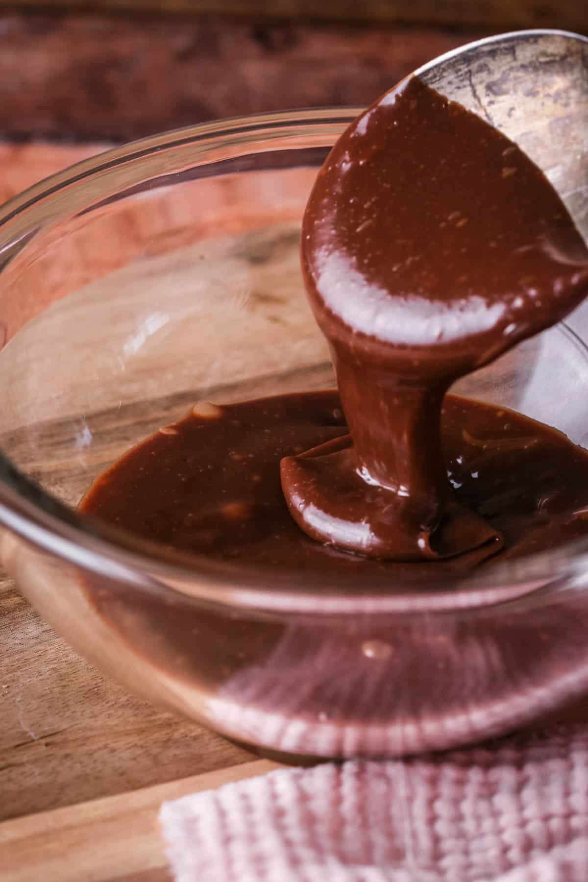 Milk Chocolate Ganache smooth and very pourable being lifted up by spoon in a bowl. Glossy and delicious looking.
