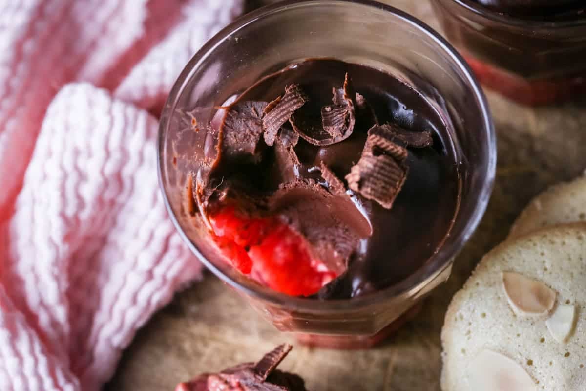 Chocolate Pots for Two with fruity raspberry bottom layer. Silky spoonful taken out showing creamy ganache inside and raspberries at the bottom.