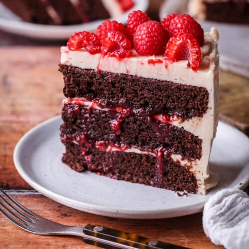 Slice of Chocolate Raspberry Cake on a plate. Moist chocolate sponge, raspberry jam squidging out of the filling.