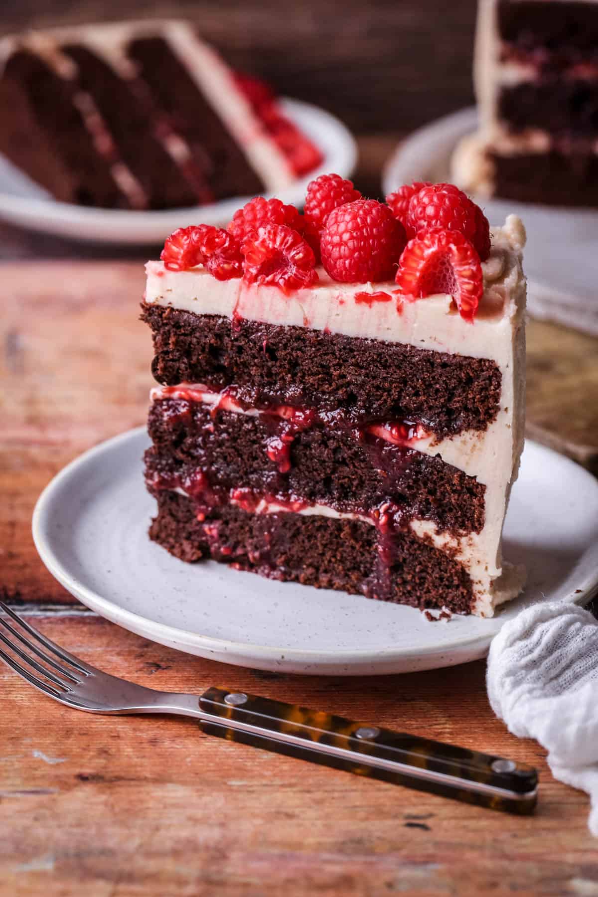 Slice of Chocolate Raspberry Cake on a plate. Moist chocolate sponge, raspberry jam squidging out of the filling.