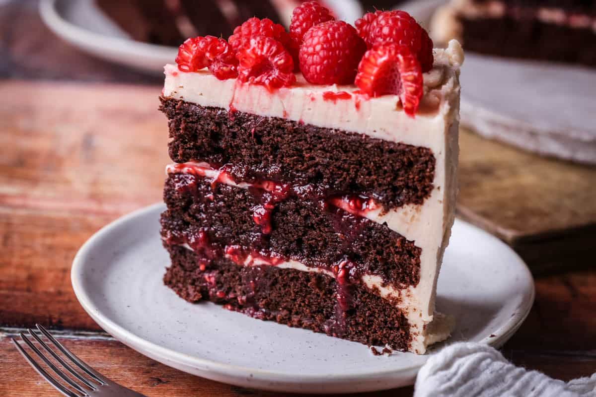 Slice of Chocolate Raspberry Cake on a plate. Moist chocolate sponge, raspberry jam squidging out of the filling.