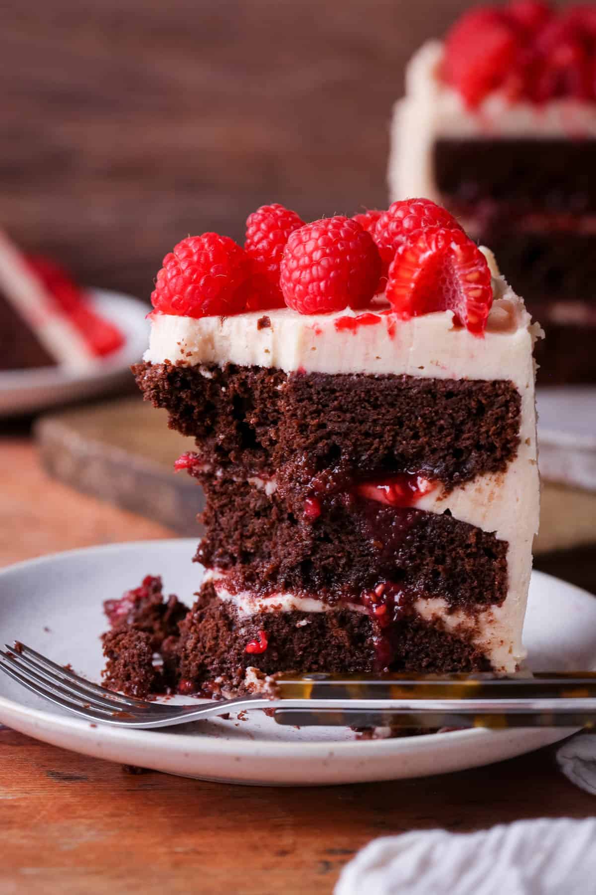 Forkful taken out of slice of Chocolate Raspberry Cake on a plate. Moist chocolate sponge, raspberry jam squidging out of the filling.