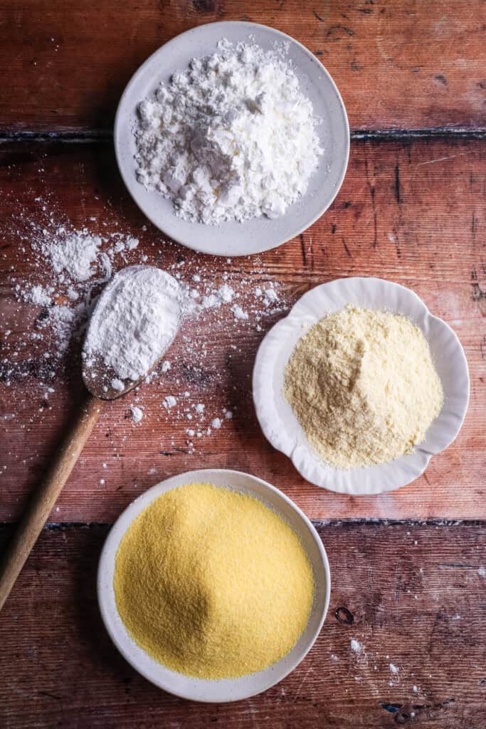 Cornflour, fine cornmeal and polenta on a table showing the differences between how they look.