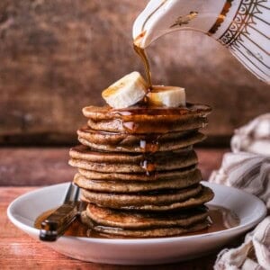 A stack of thick, soft and fluffy banana pancakes. Topped with bananas and drizzled with maple syrup.