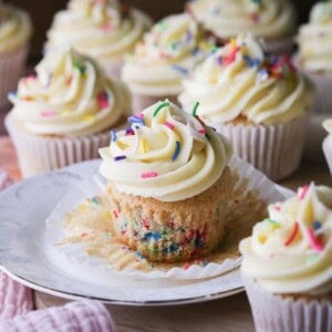 Gluten-Free Funfetti Cupcake on a plate with the liner removed showing the soft tender fluffy crumb which is packed with colourful sprinkles.