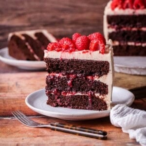 Slice of Chocolate Raspberry Cake on a plate. Moist chocolate sponge, raspberry jam squidging out of the filling.