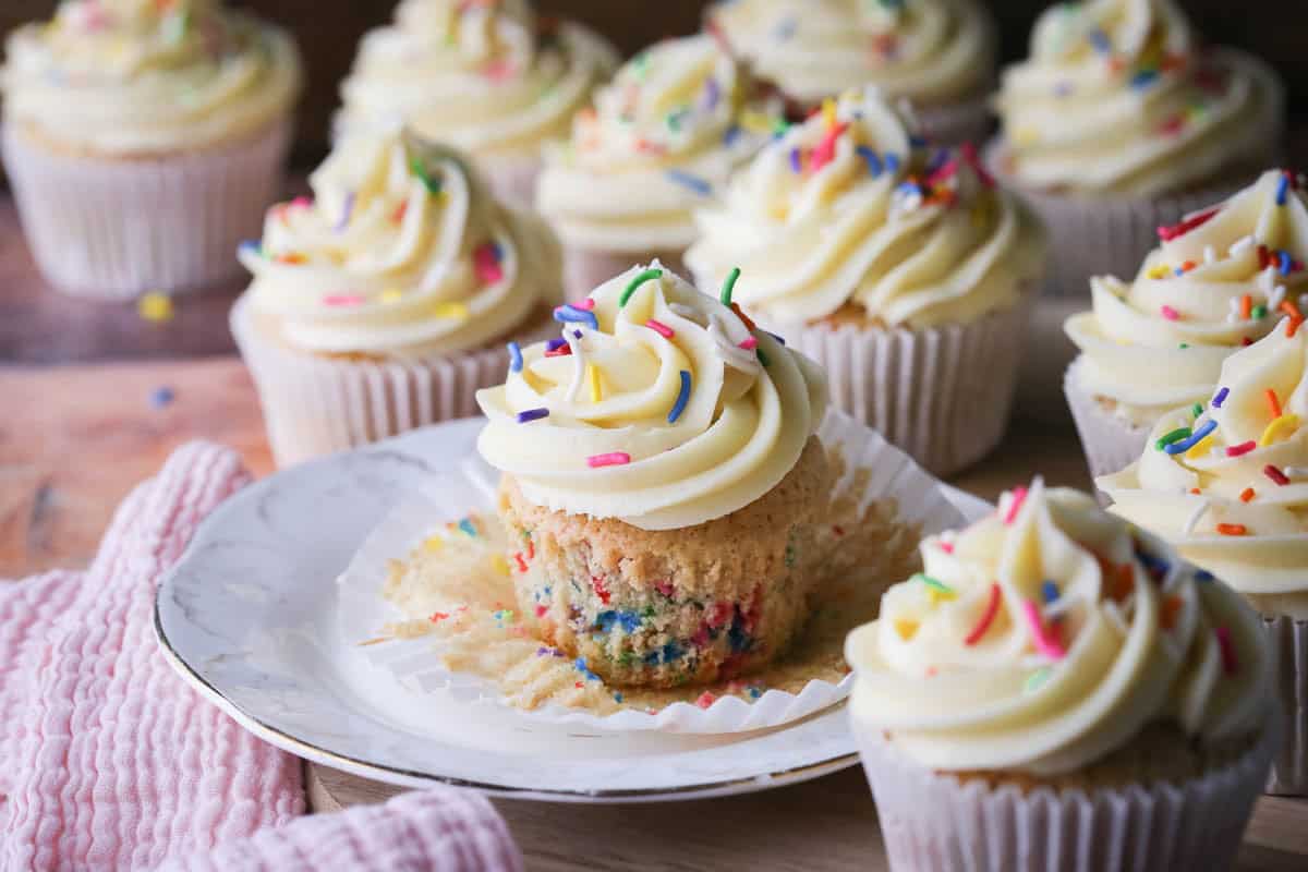 Gluten-Free Funfetti Cupcake on a plate with the liner removed showing the soft tender fluffy crumb which is packed with colourful sprinkles.