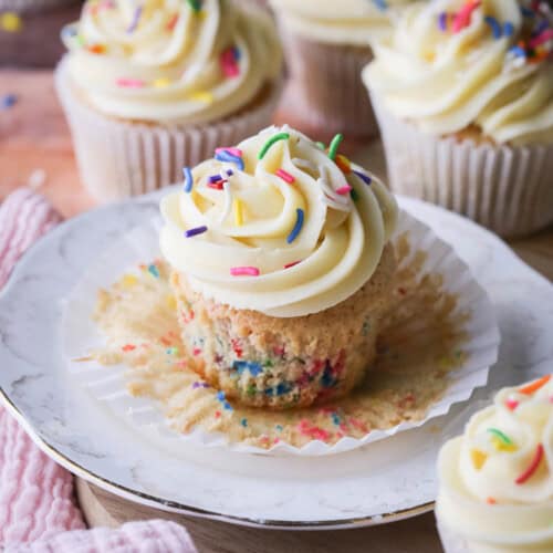 Gluten-Free Funfetti Cupcake on a plate with the liner removed showing the soft tender fluffy crumb which is packed with colourful sprinkles.