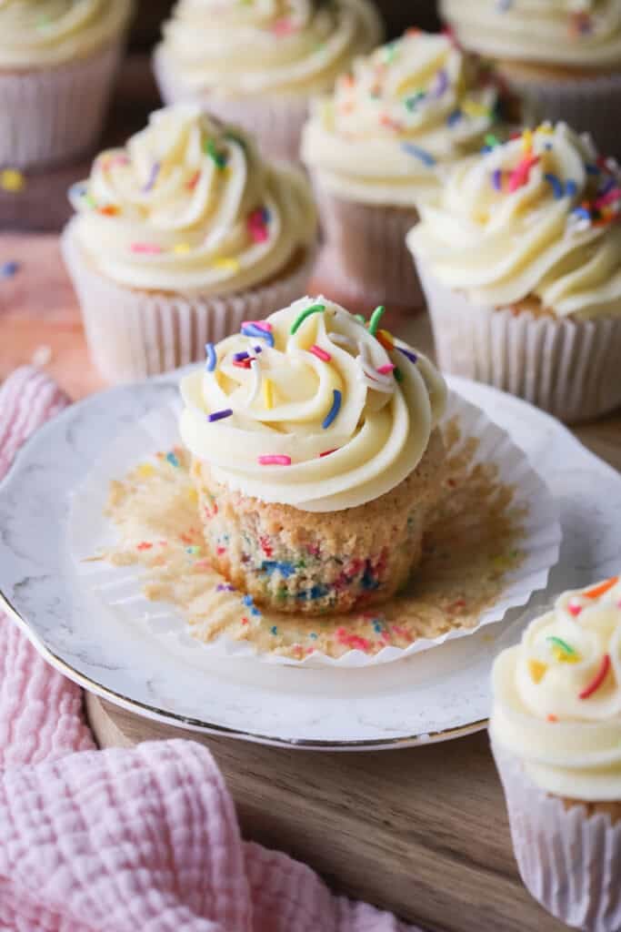 Gluten-Free Funfetti Cupcake on a plate with the liner removed showing the soft tender fluffy crumb which is packed with colourful sprinkles.