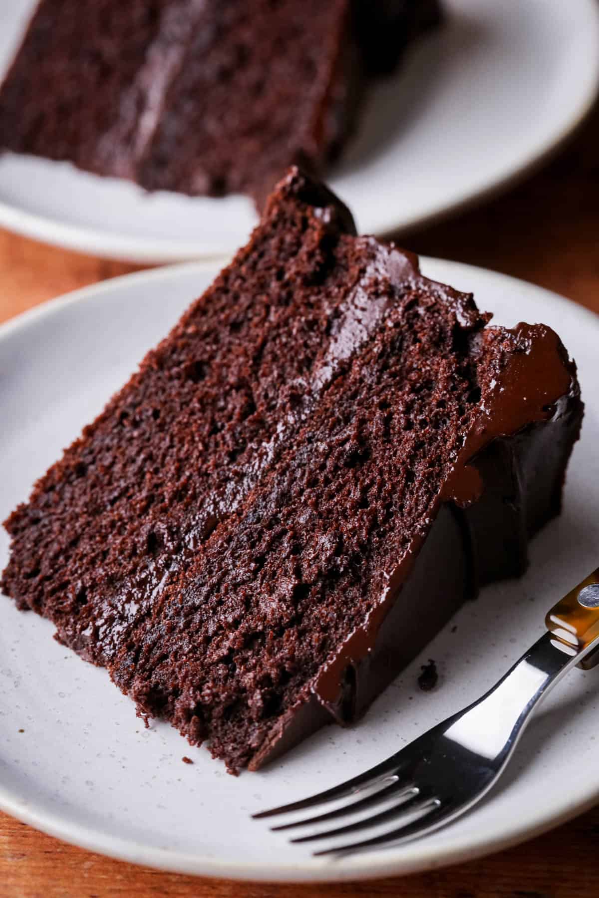Slice of Chocolate fudge cake on plate showing soft moist sponge and richly intense creamy ganache.