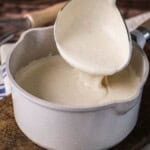 Béchamel in a saucepan with large ladle scooping some up showing how lusciously thick and creamy it is.